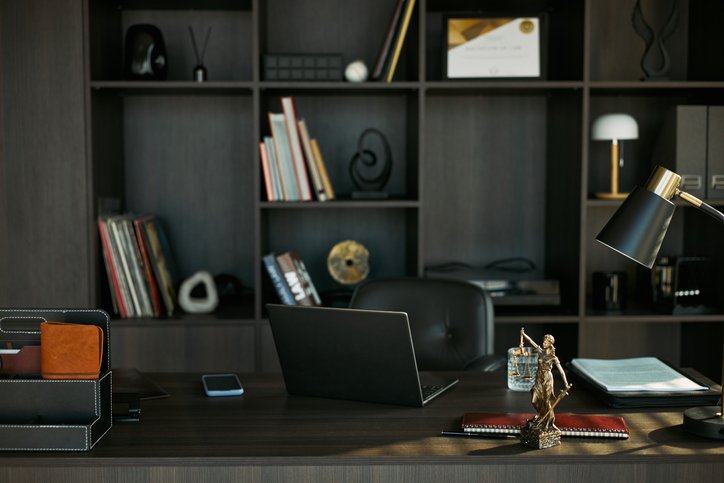 Law Office Workspace Representing Divorce Legal Consultation Modern office desk with an open laptop, desk lamp, notebooks, and a bronze statue on a dark wood surface.